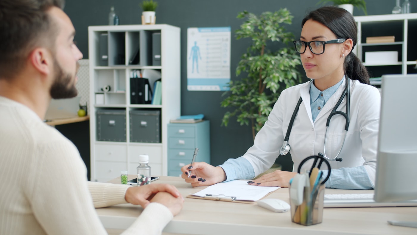 A clinician in a thoughtful consultation with an older adult in an office.